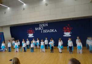 Dzieci tańczą z białymi i niebieskimi wstążkami.