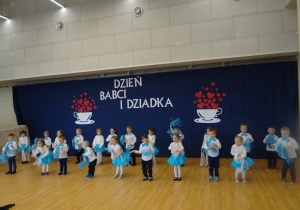 Dzieci tańczą z białymi i niebieskimi wstążkami.