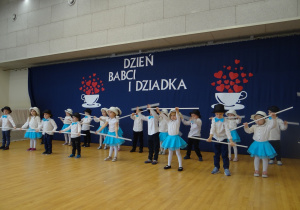 Dzieci tańczą w kapeluszach, trzymając w rękach białą laskę.