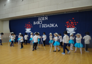 Dzieci tańczą w kapeluszach, trzymając w prawej ręce białą laskę.