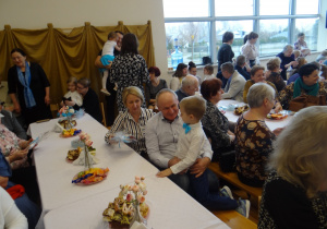 Dziadkowie siedzą za stołem i dziękują wnuczkowi za prezent.