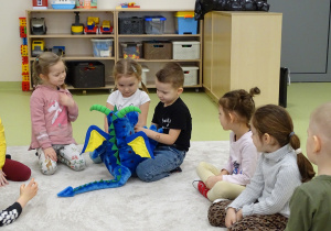 Dzieci oglądają niebieskiego, pluszowego smoka.