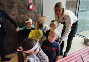 Dzieci z opaskami w kształcie pizzy na głowie stoją w odpowiednich grupkach.
