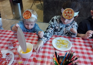 Dzieci ozdabiają swoją papierową pizzę.