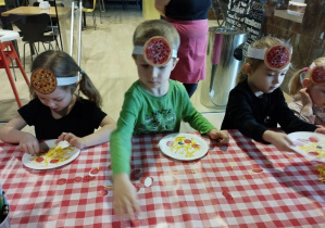 Dzieci ozdabiają swoją papierową pizzę.