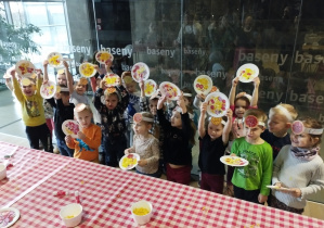Dzieci pokazują swoje ozdobione papierowe pizze.