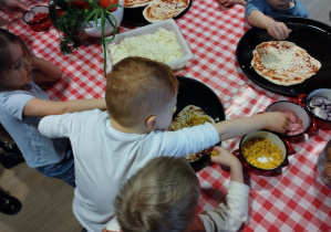 Dzieci kładą na pizzę swoje ulubione dodatki.