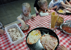 Dzieci kładą na pizzę swoje ulubione dodatki.