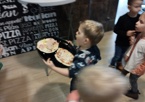 Chłopiec niesie pizzę do pieca.