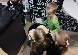 Dzieci niosą pizzę do pieca.