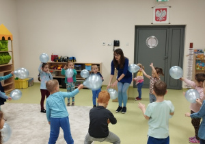 Dzieci z panią tańczą z błękitnymi balonami.