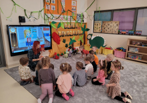 Dzieci siedzą w kole pani animuje pacynką dinozaura