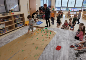 Dziecko idzie po papierze robiąc ślady stopami pomalowanymi farbą