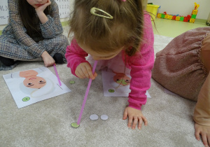 Dziewczynka przenosi słomką małe, papierowe ogórki.