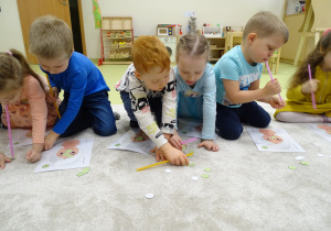 Dzieci przenoszą słomką małe, papierowe ogórki.