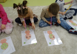 Dzieci przenoszą słomką małe, papierowe ogórki.