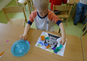 Chłopiec przykleja na szablon kolorowe piórka.