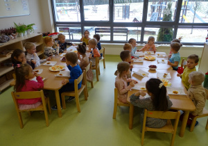 Dzieci zajadają się przy stolikach babeczkami i owocami.