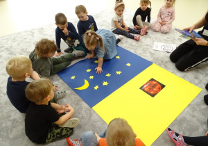 Dzieci układają gwiazdki i księżyc na ciemnym kartonie