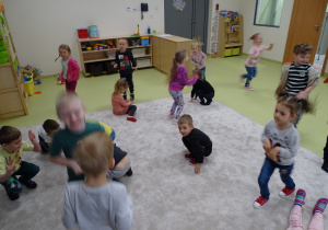 Dzieci uczestniczą w zabawie ruchowej na dywanie.