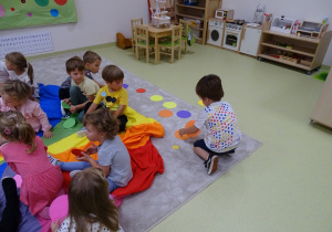 Dzieci zbierają z podłogi kółeczka w kolorze kawałka chusty na którym siedzieli