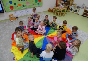 Dzieci siedzą na chuście trzymając kolorowe kółeczka