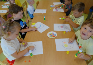 Dzieci robią pracę plastyczną używając kolorowych kółeczek
