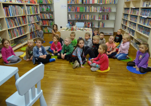 Dzieci siedzą na podłodze pomiędzy regałami książek.