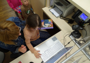Dziewczynka wprowadza książkę do komputerowego systemu bibliotecznego.