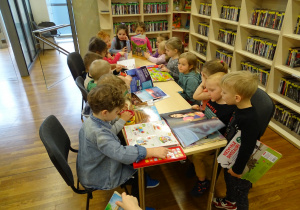 Dzieci czytają książki przy stolikach.