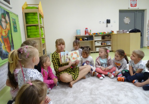 Dzieci siedzą z panią bibliotekarką w kole. Pani czyta książkę.