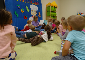 Dzieci siedzą w kole. Pani czyta dzieciom książkę.