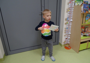 Chłopiec trzyma znalezioną przez siebie kopertę i kolorowe jajo.