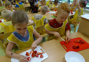 Dzieci kroją owoce na tackach.
