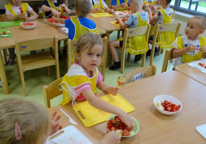 Dzieci nadziewają owoce na wykałaczki robiąc szaszłyki.