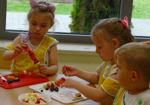 Dzieci nadziewają owoce na wykałaczki robiąc szaszłyki.