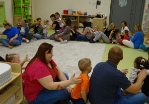 Dzieci i rodzice siedzą w kole plecy za plecami i dotykają pleców.