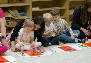 Dzieci z rodzicami pochylają się nad kartkami z biedronkami i kropeczkami licząc je.