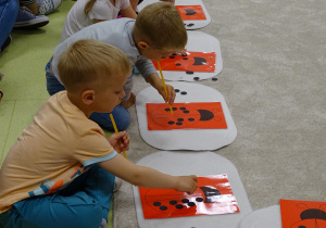 Dzieci pochylają się nad kartkami z biedronkami i kropeczkami przeciągając je za pomocą słomki.