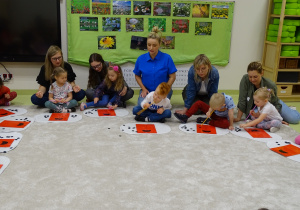 Dzieci z rodzicami pochylają się nad kartkami z biedronkami i kropeczkami licząc je i przeciągając za pomocą słomki.