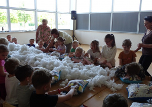 Dzieci wypychają poduszkę białym puchem.