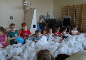 Dzieci wypychają poduszkę białym puchem.