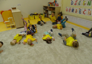 Dzieci bawią się w śmiechojogę i leżą na podłodze machając nogami.