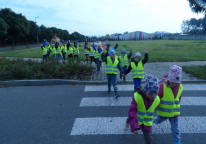 Dzieci idą przez pasy podnosząc ręce do góry.