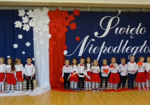 Dzieci stoją na tle biało - czerwonej dekoracji.
