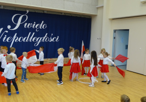 Dzieci tańczą z białymi i czerwonymi chustkami i biało - czerwonymi flagami.
