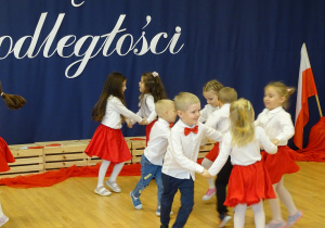 Dzieci tańczą w trójkach trzymając się za ręce.