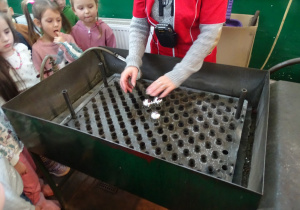 Dzieci oglądają maszyny do malowania srebrem wnętrza bombek.