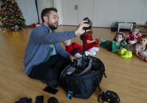Pan pokazuje dzieciom siedzącym na podłodze aparat.