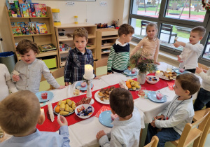 Dzieci stoją przy stole z kawałkiem opłatka w dłoni